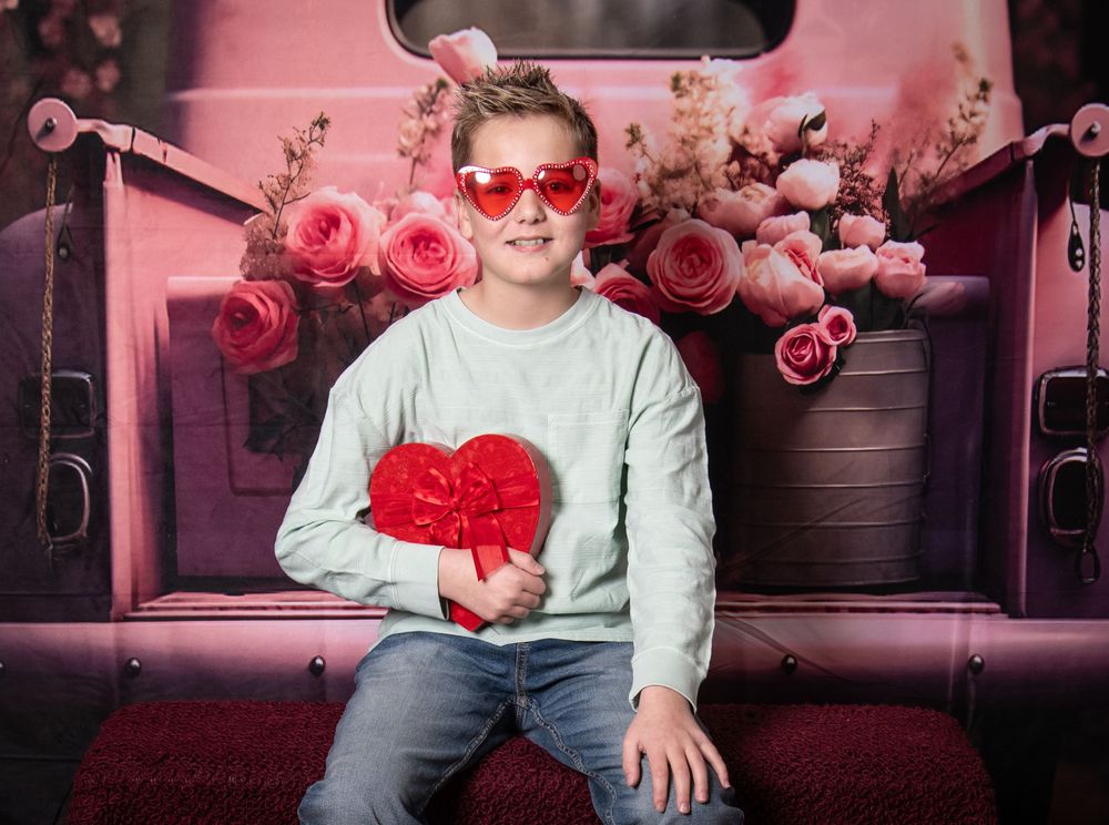 A romantic Valentine's Day photo shoot setup in a pink-lit vintage car interior with rose decorations.