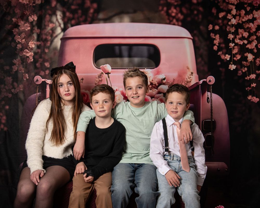 A family portrait session against a dark background with pink cherry blossoms creating a dreamy atmosphere.