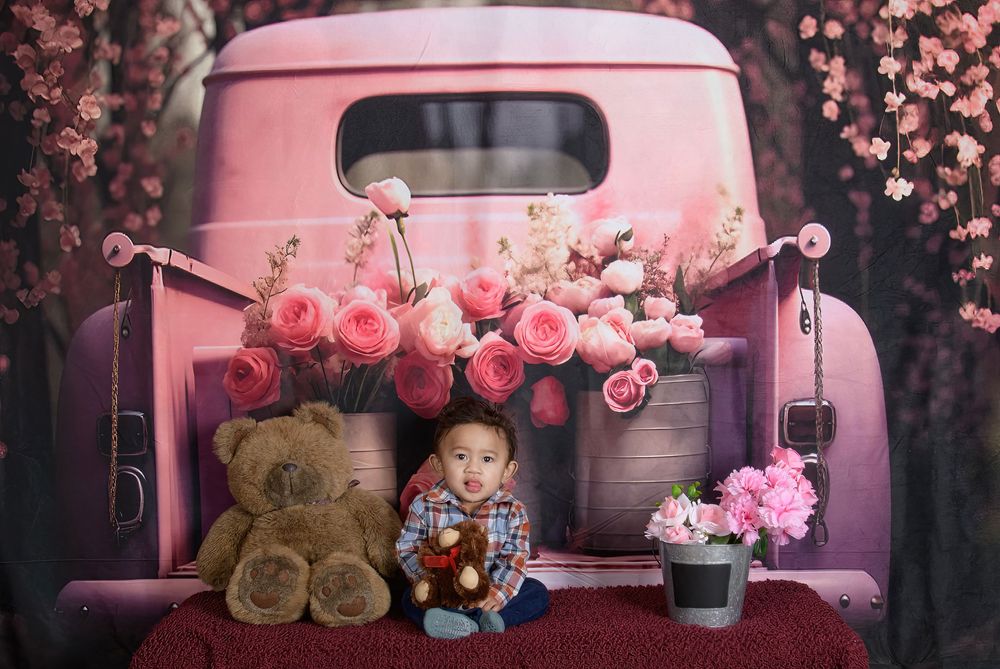 A pink vintage car surrounded by blooming cherry blossoms and roses creates a dreamy romantic scene.