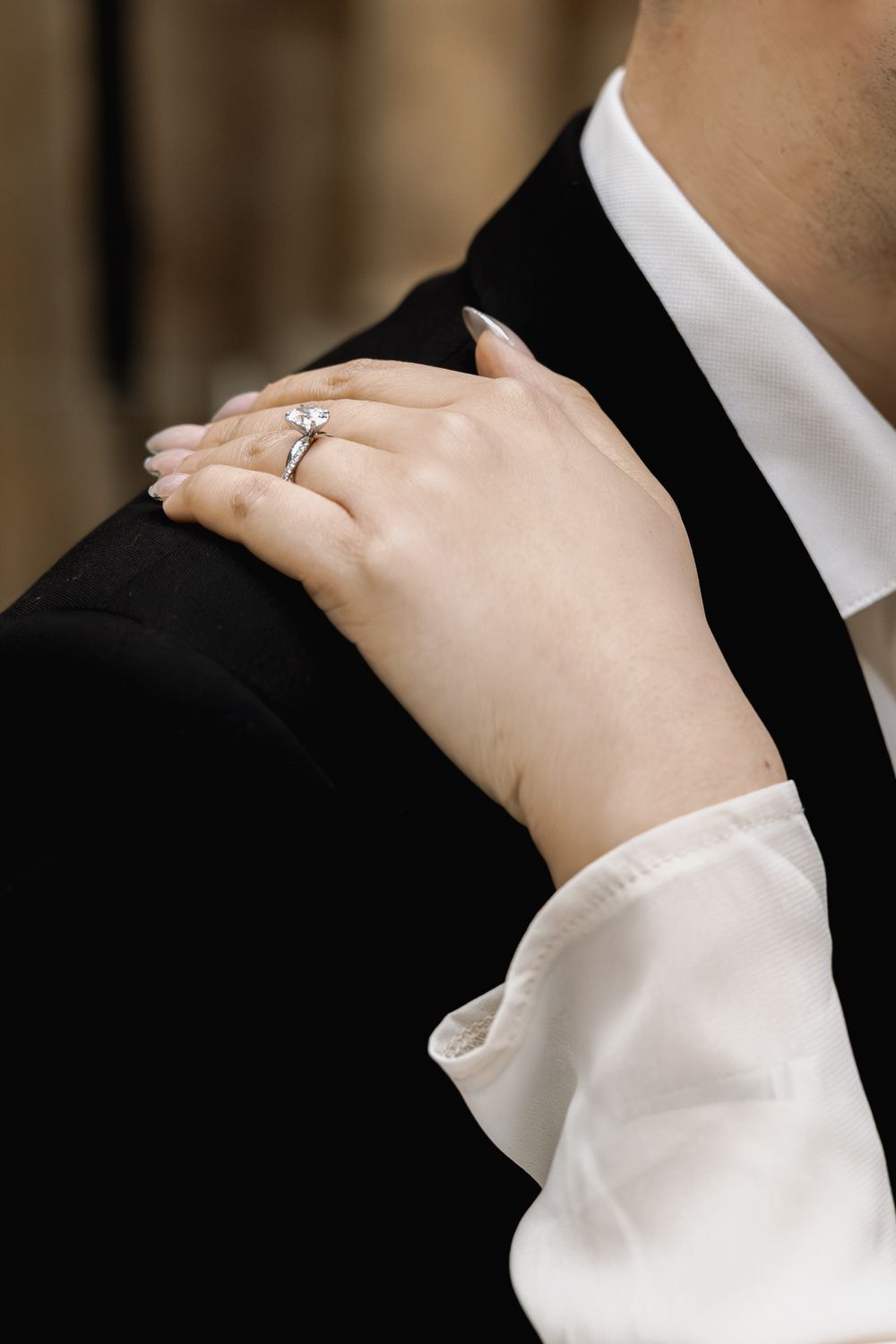 Close-up view of hands adjusting a white dress shirt collar against a dark suit jacket in formal attire.