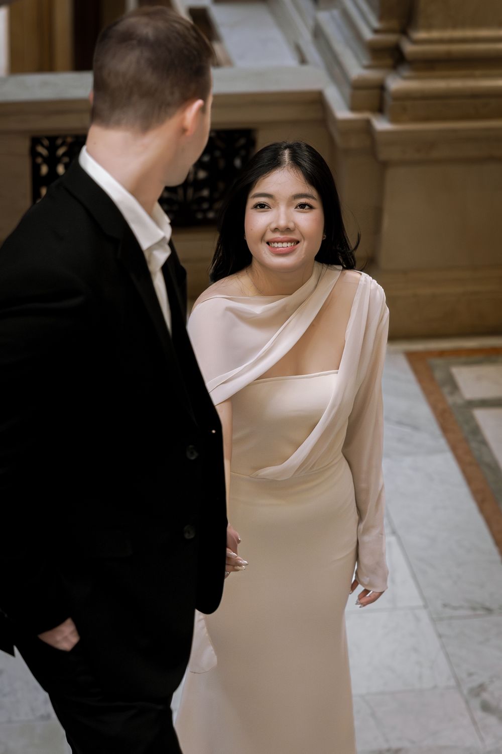 Elegant couple in formal attire sharing intimate moments during a wedding photoshoot in a grand hallway.