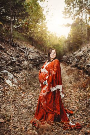 Dramatic maternity portrait on rocky terrain wearing a flowing red dress with autumn scenery.