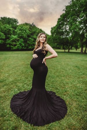 A flowing black dress twirls dramatically against a green lawn during a maternity photoshoot.