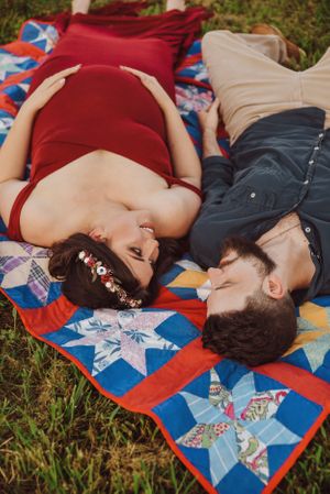 Couple lying on a colorful patchwork quilt during an outdoor photo session.