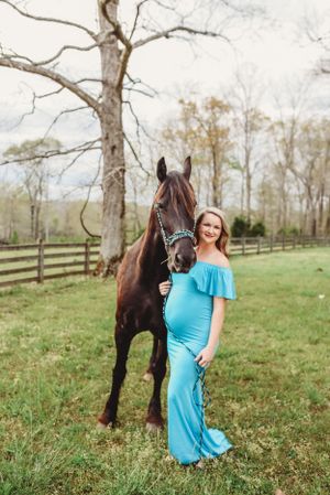 A beautiful brown horse stands beside someone wearing a flowing turquoise dress in a pastoral field setting.