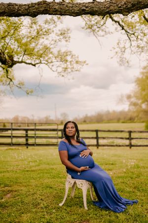 A maternity portrait session in a rustic field with wooden fence and tree backdrop.