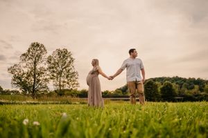 A couple walks through a scenic field at sunset with dramatic clouds overhead.