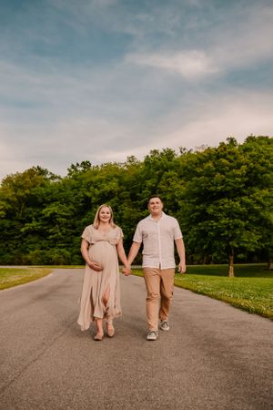A couple holds hands while walking on a paved path surrounded by green landscape.