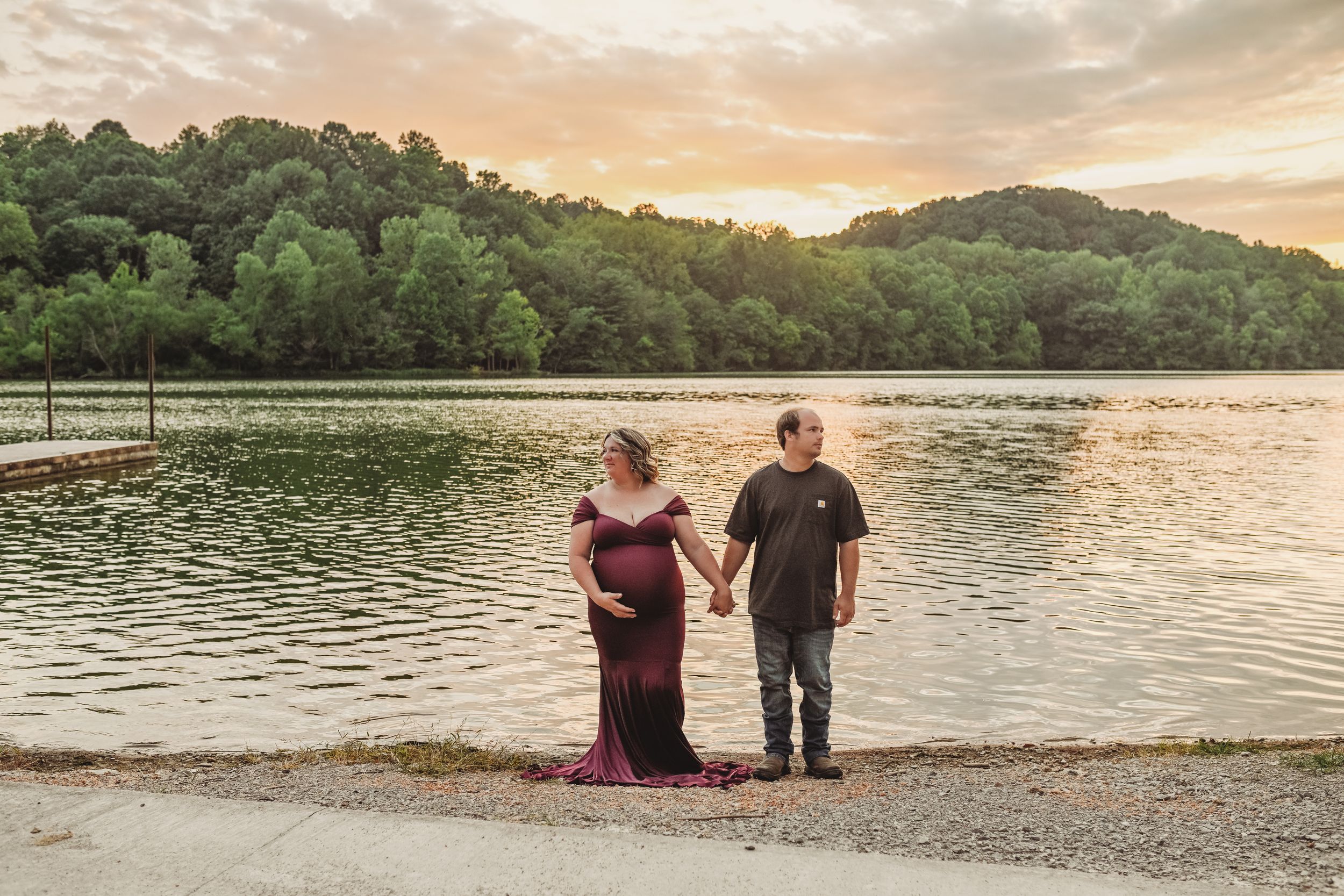 A couple stands at the edge of a lake during sunset.