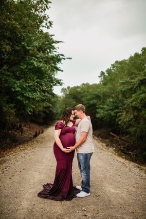 A couple shares an intimate moment on a gravel path surrounded by green trees.