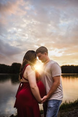 Intimate sunset maternity photo by lake with dramatic sky backdrop.