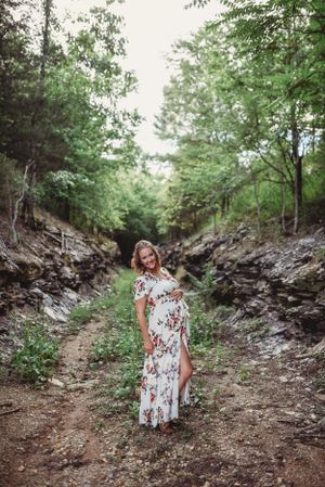 Maternity photo in a rocky ravine wearing a flowing white floral dress.