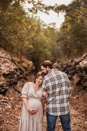 Expecting couple shares intimate moment on wooded trail during sunset maternity photoshoot.