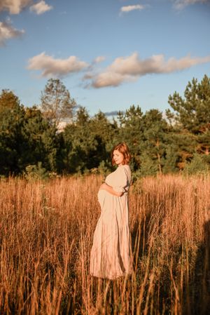Golden hour maternity photo in tall grass field with soft natural lighting.