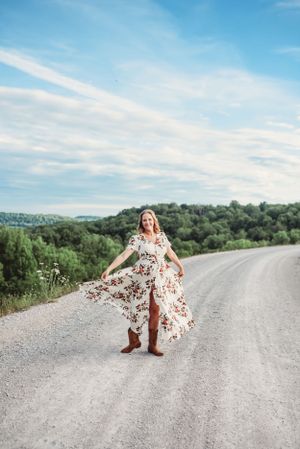A flowing floral dress twirls on a country road with rolling hills in the background.