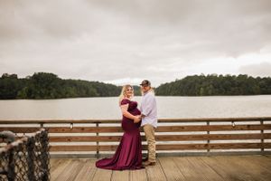 Romantic lakeside maternity photo on wooden deck during overcast day.