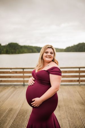 Joyful maternity portrait on wooden pier overlooking serene lake.