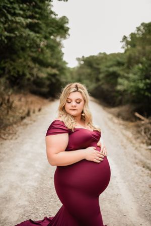 Stunning maternity portrait on rustic dirt path with form-fitting burgundy gown.