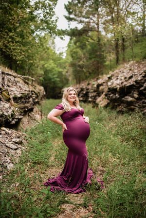 Elegant maternity photo featuring burgundy dress against dramatic rocky landscape.