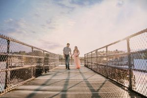 Two people walk along a wooden bridge over water during sunset.