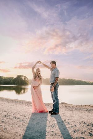 A couple shares tender moments on a beach at sunset with soft pink skies.