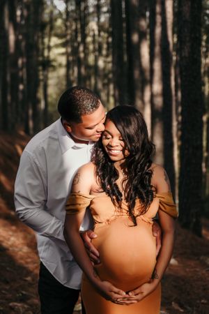 Intimate maternity photoshoot in a forest setting with warm lighting and natural surroundings.