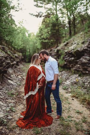 Couple embracing on rocky forest path with flowing red vintage dress.