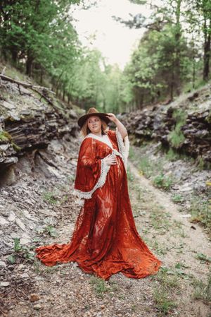 Person in red lace dress poses gracefully on rocky forest path.