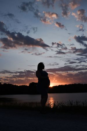 Silhouetted figures stand by a lake during sunset with dramatic clouds in the sky.