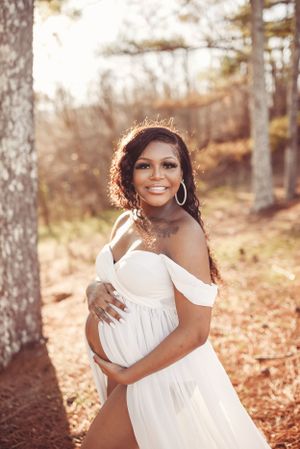 Glowing sunset maternity portrait in a forest setting with off-shoulder white dress.