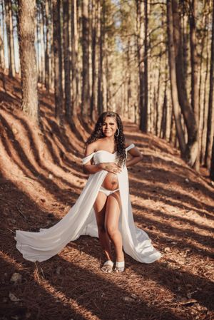 Dramatic forest photoshoot with flowing white gown creating movement among tall pine trees.