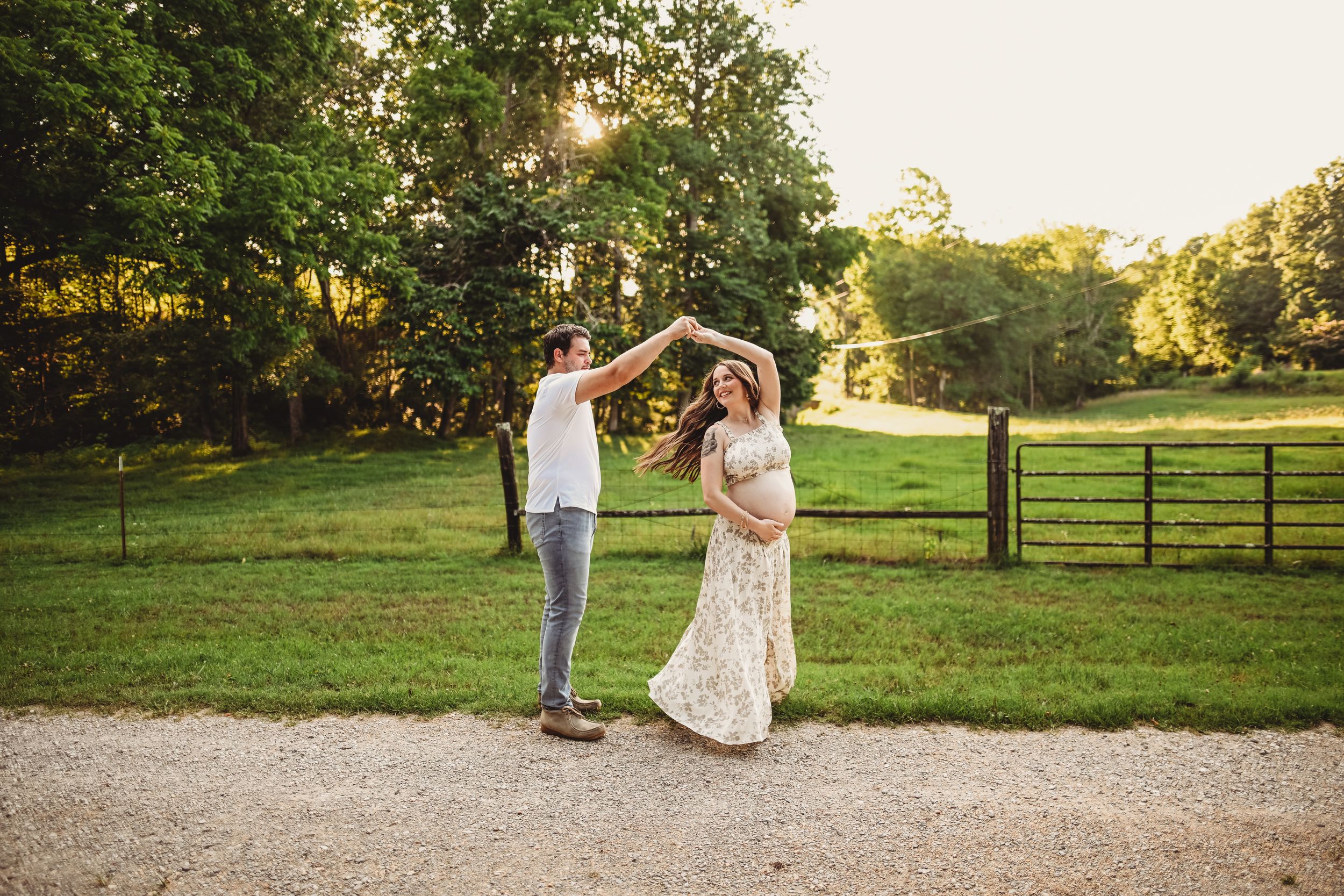 A couple dancing together in a scenic field at sunset.