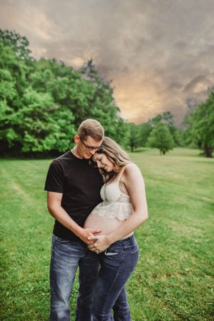A couple shares an intimate moment outdoors while expecting a baby on a cloudy evening.