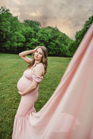 A flowing pink maternity dress catches the evening light in an outdoor photo session.
