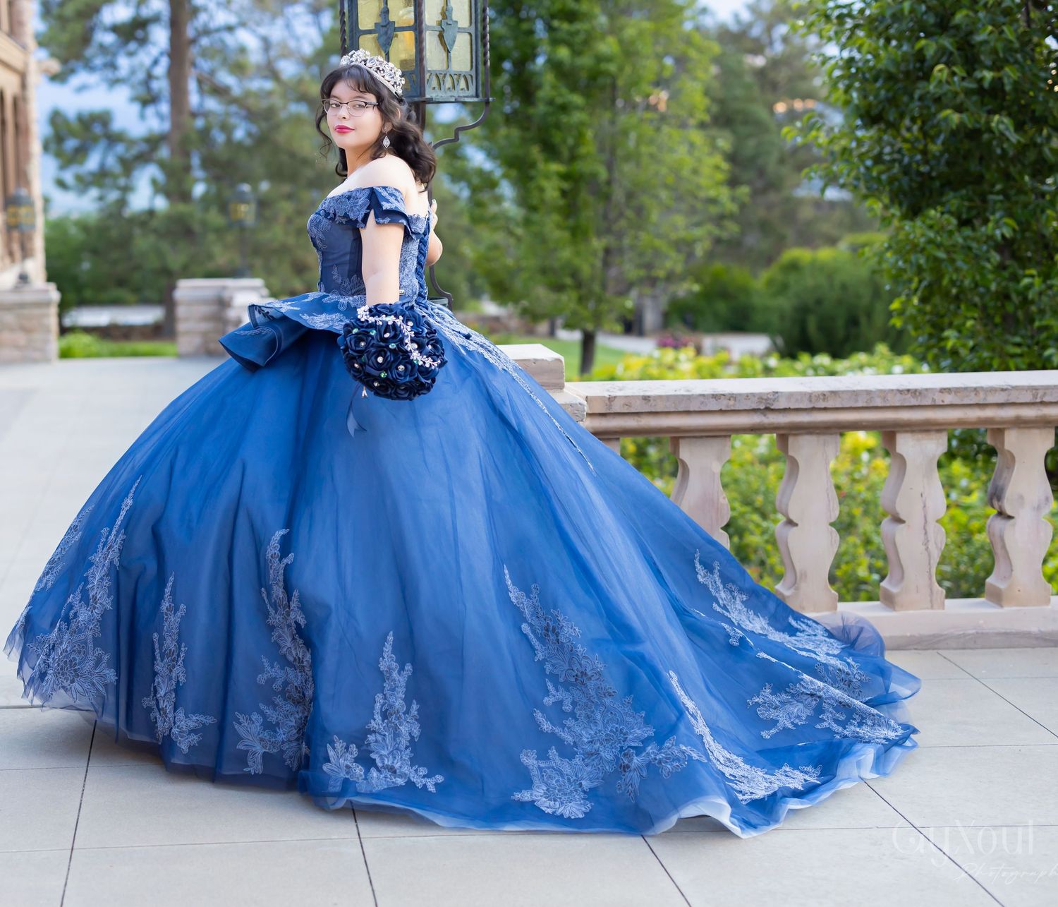 Stunning royal blue ball gown with intricate lace details and full tulle skirt photographed on balcony with garden view.