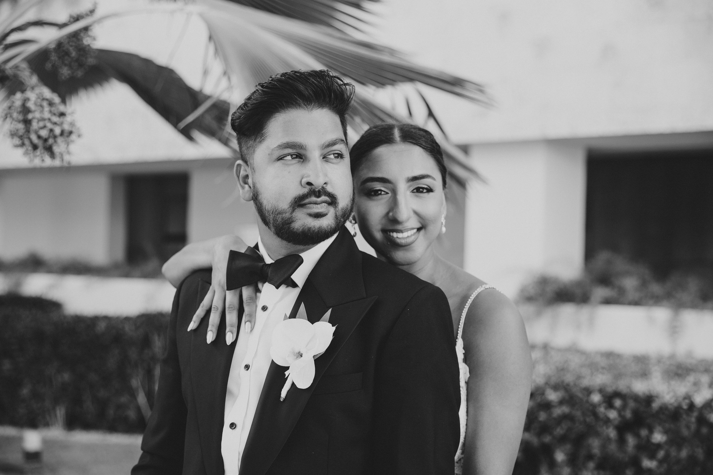 Black and white portrait of newlyweds smiling against a tropical backdrop.