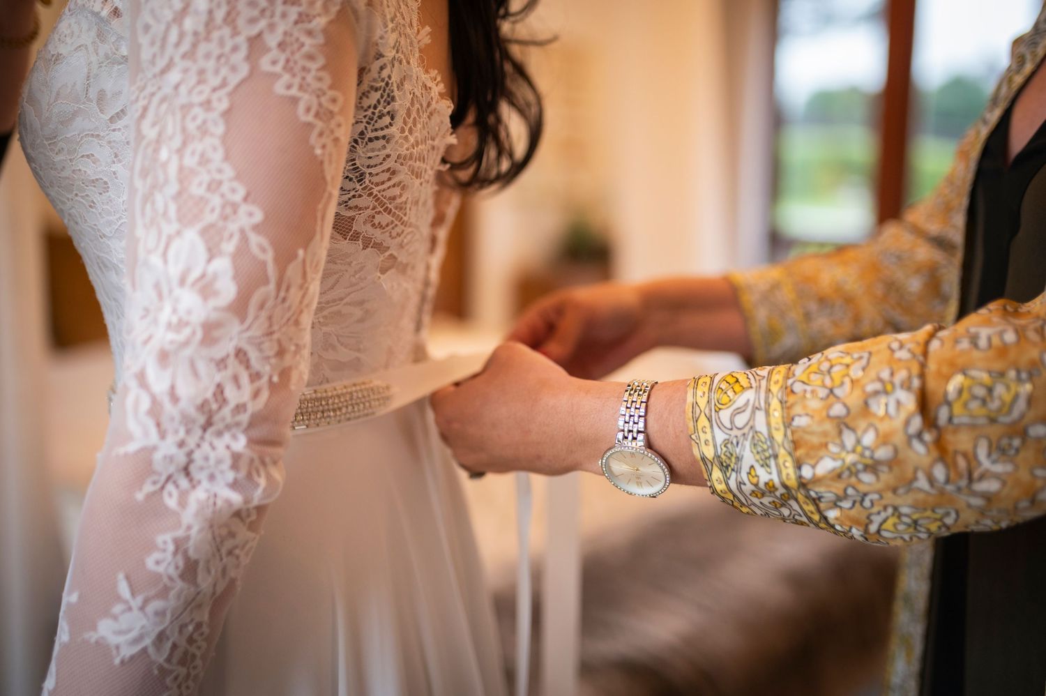 Close-up of delicate lace wedding dress being adjusted, showing intricate sleeve detail and sparkly bracelet.
