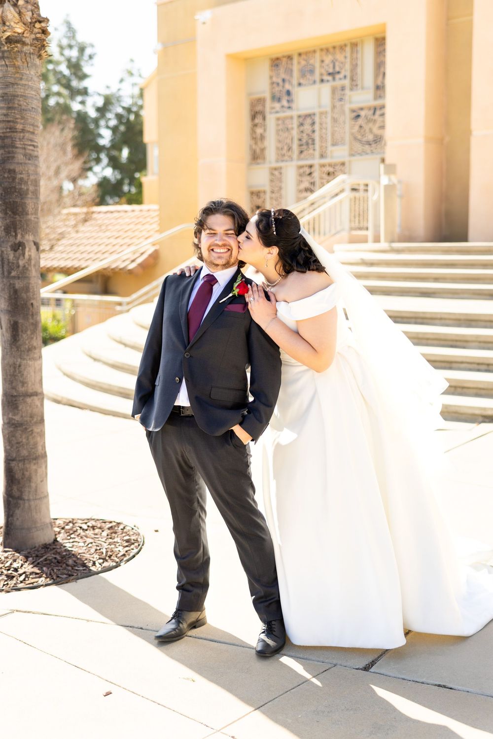 A romantic wedding moment captured on stone steps with a classic yellow-walled building in the background.