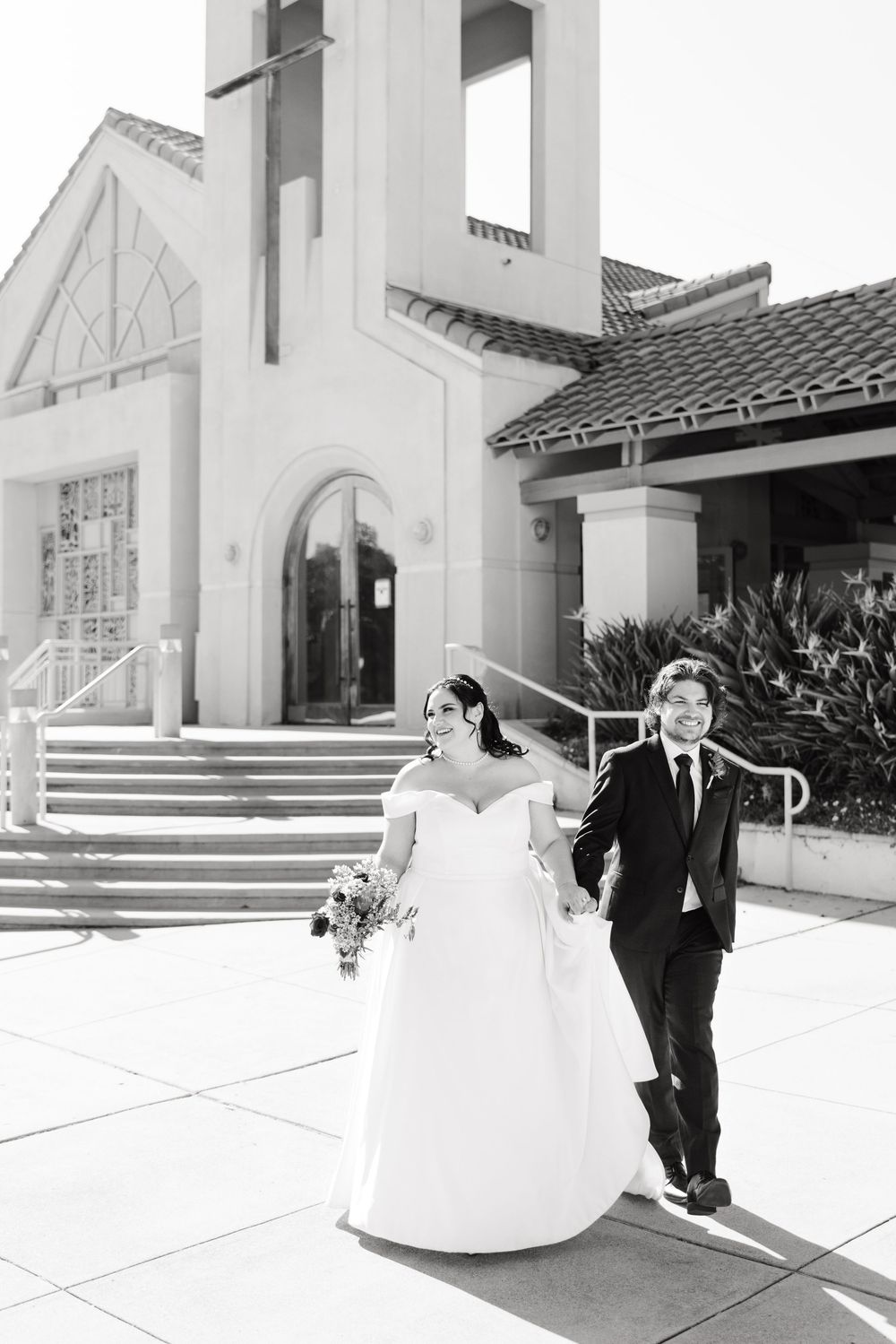 A series of five black and white wedding photos showing a couple playfully walking outside a mission-style church.