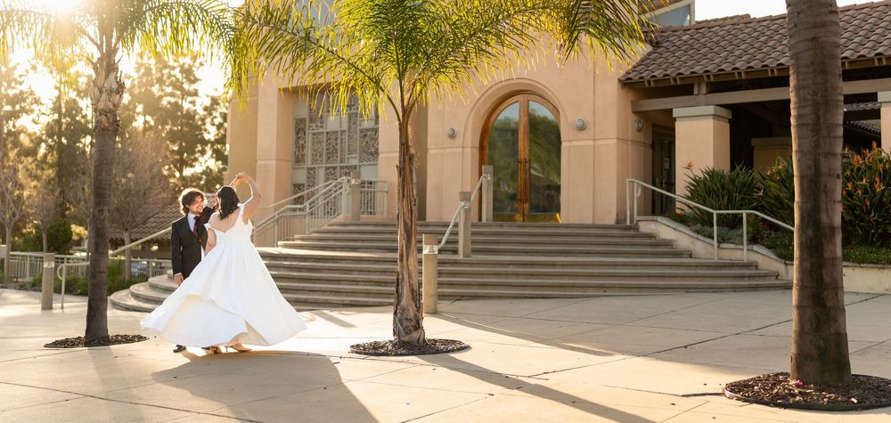 Sun-drenched wedding photograph outside a Mediterranean-style building with palm trees and curved stone steps.