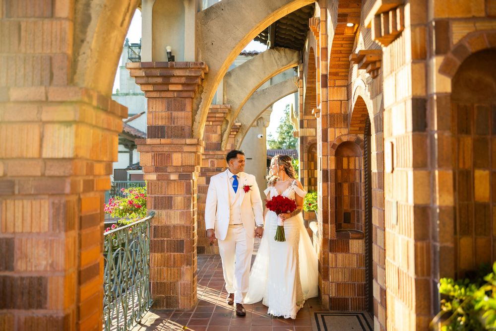 Beautiful wedding couple walks along a stone archway corridor during golden hour.