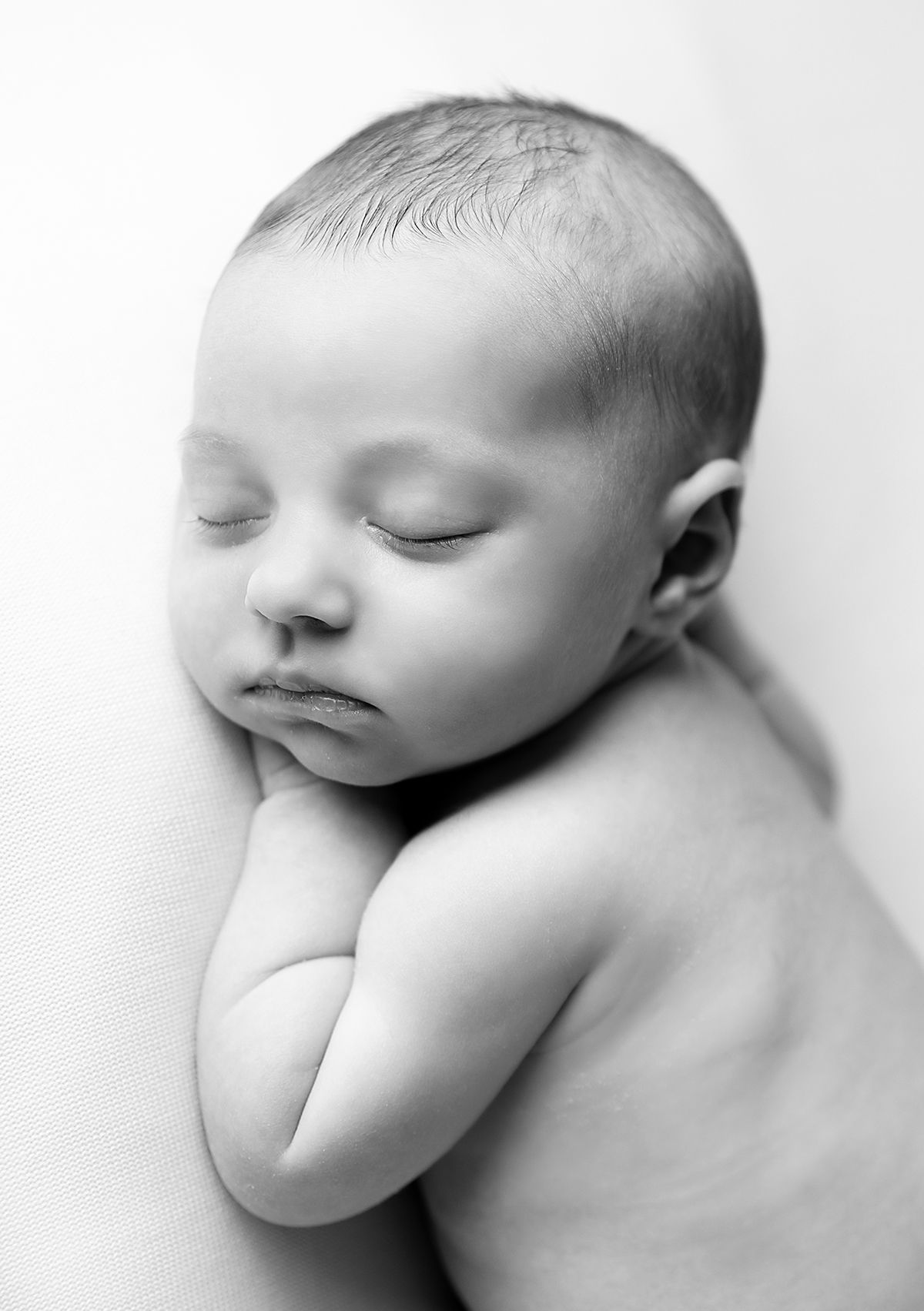 A peaceful sleeping newborn baby curled up on side in black and white artistic portrait photography. During a newborn session in Bexley