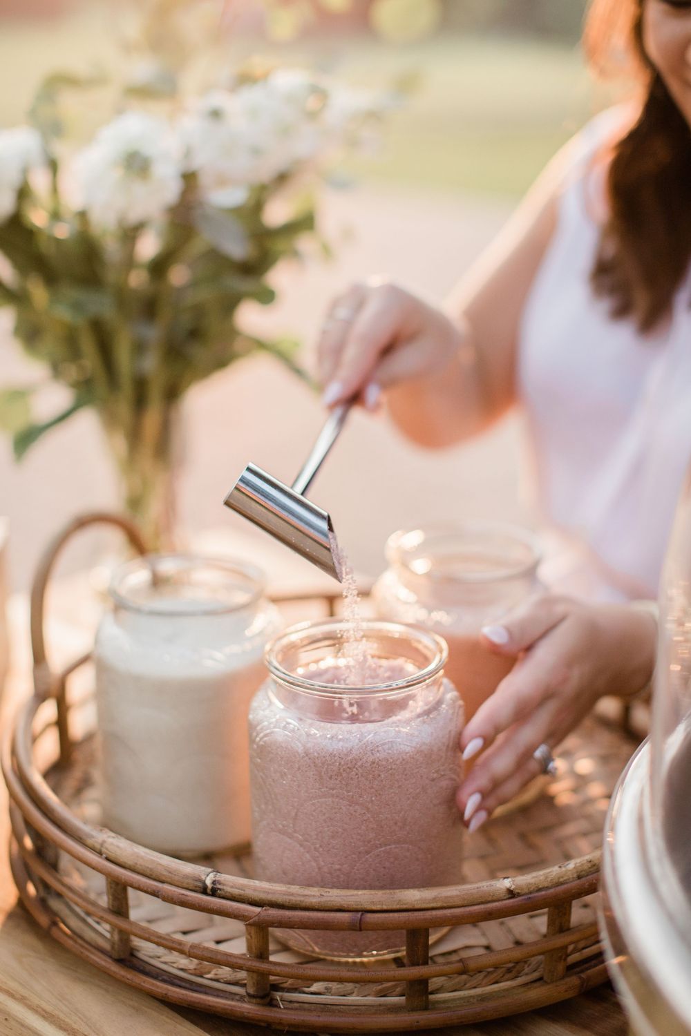 Pink and white milkshakes topped with whipped cream are served on a wooden tray in warm natural lighting.