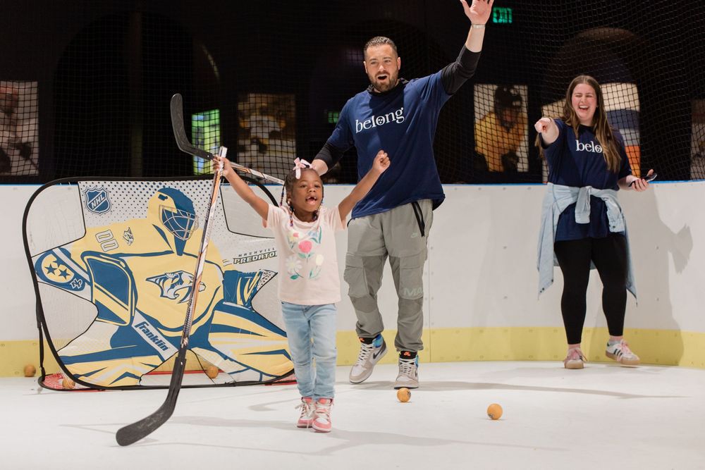 People playing broomball on an ice rink, running and sliding with brooms and a ball during a recreational game.