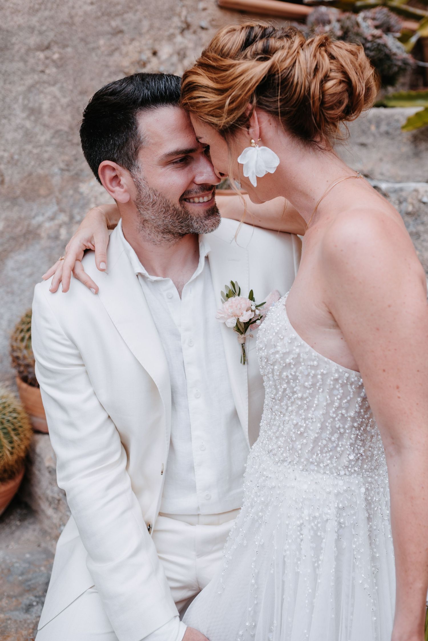 Eine romantische Fotoserie von einer Hochzeit zeigt ein Paar in weißer Kleidung, das vor einer rustikalen Steinmauer intime Momente teilt.