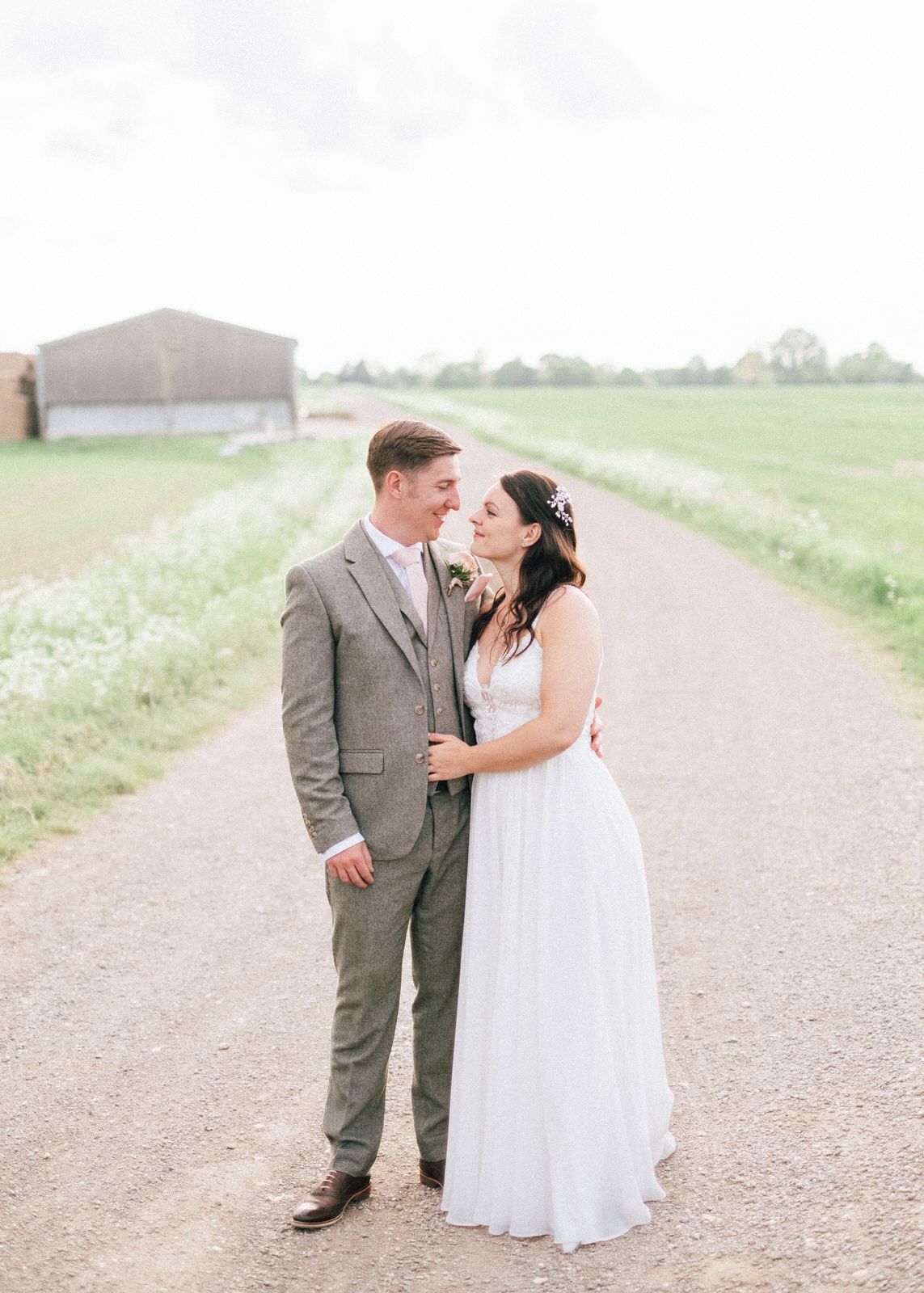Happy couple embraces and laughs together on a country dirt road in a rustic wedding photoshoot.