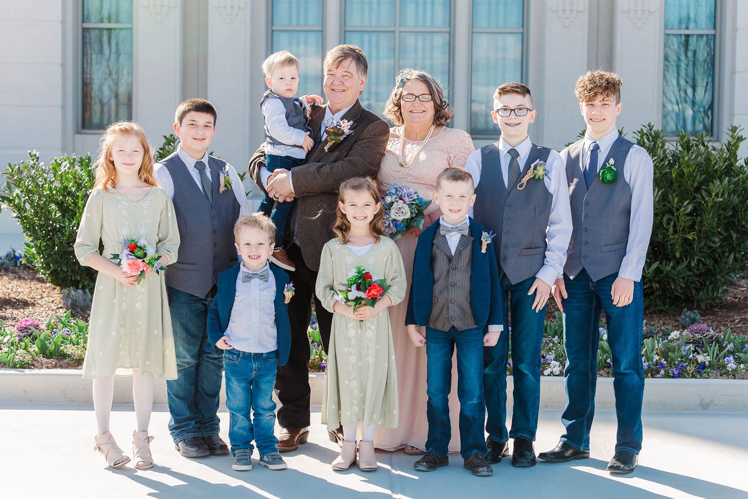Wedding party members in formal attire pose together in a line outside a building.