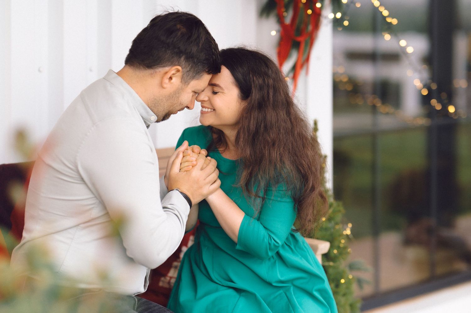 Cozy indoor holiday photoshoot with christmas lights and decorative greenery in background.