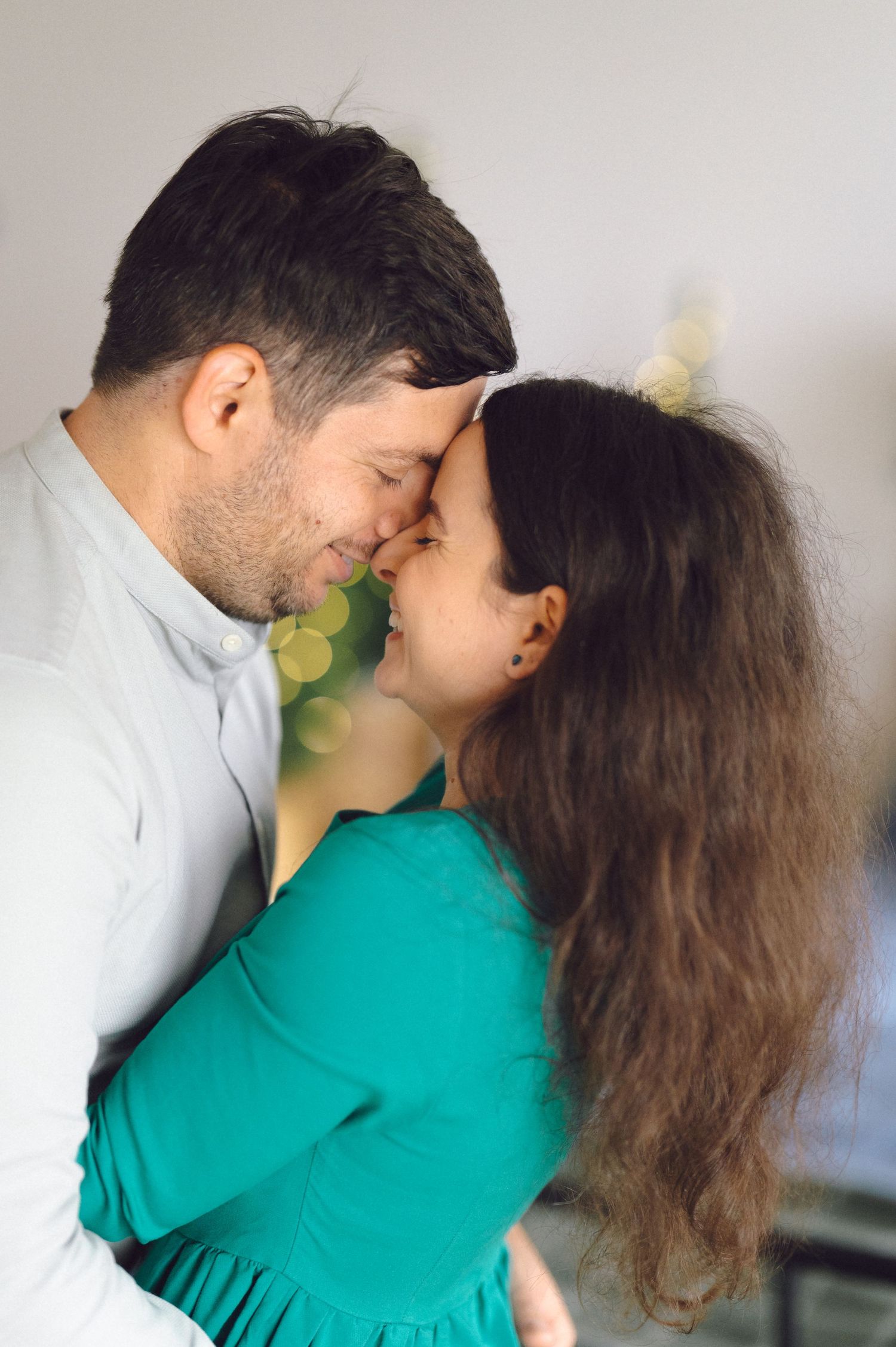 A tender romantic moment captured between a couple in a white shirt and teal dress as they lean in close together.