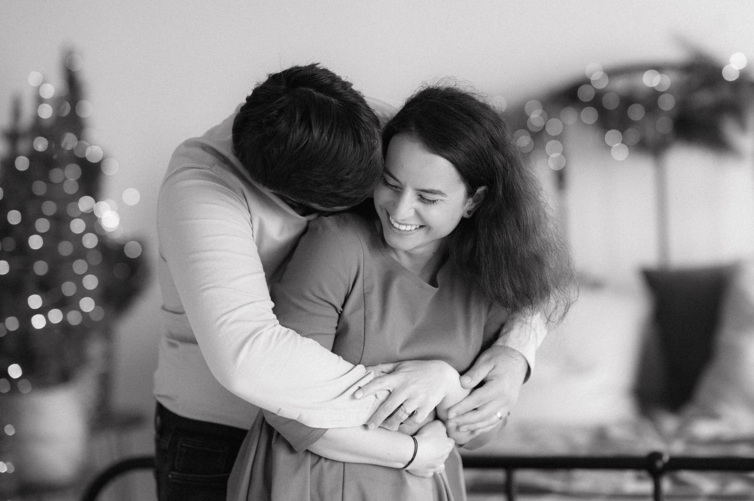 A tender black and white intimate moment shared between a couple with Christmas decorations in the background.